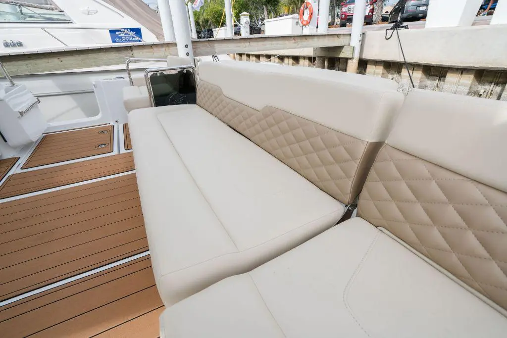 A plush beige boat sofa with diamond stitching, set against a wooden deck and marina backdrop.